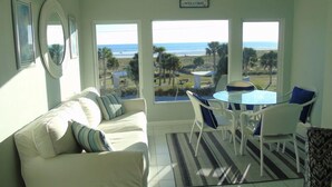 A room with a white sofa, a glass table with chairs, and a view of the beach. - Elegant condo with beach views - Sunset Royale 314 (Siesta Key)