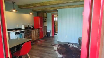 A compact kitchen with a stove, sink, and red cabinets. A dining table with red chairs is positioned in front of the kitchen.