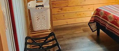 A wooden cabin room with a bed, a window, a drying rack, and a red fire extinguisher.