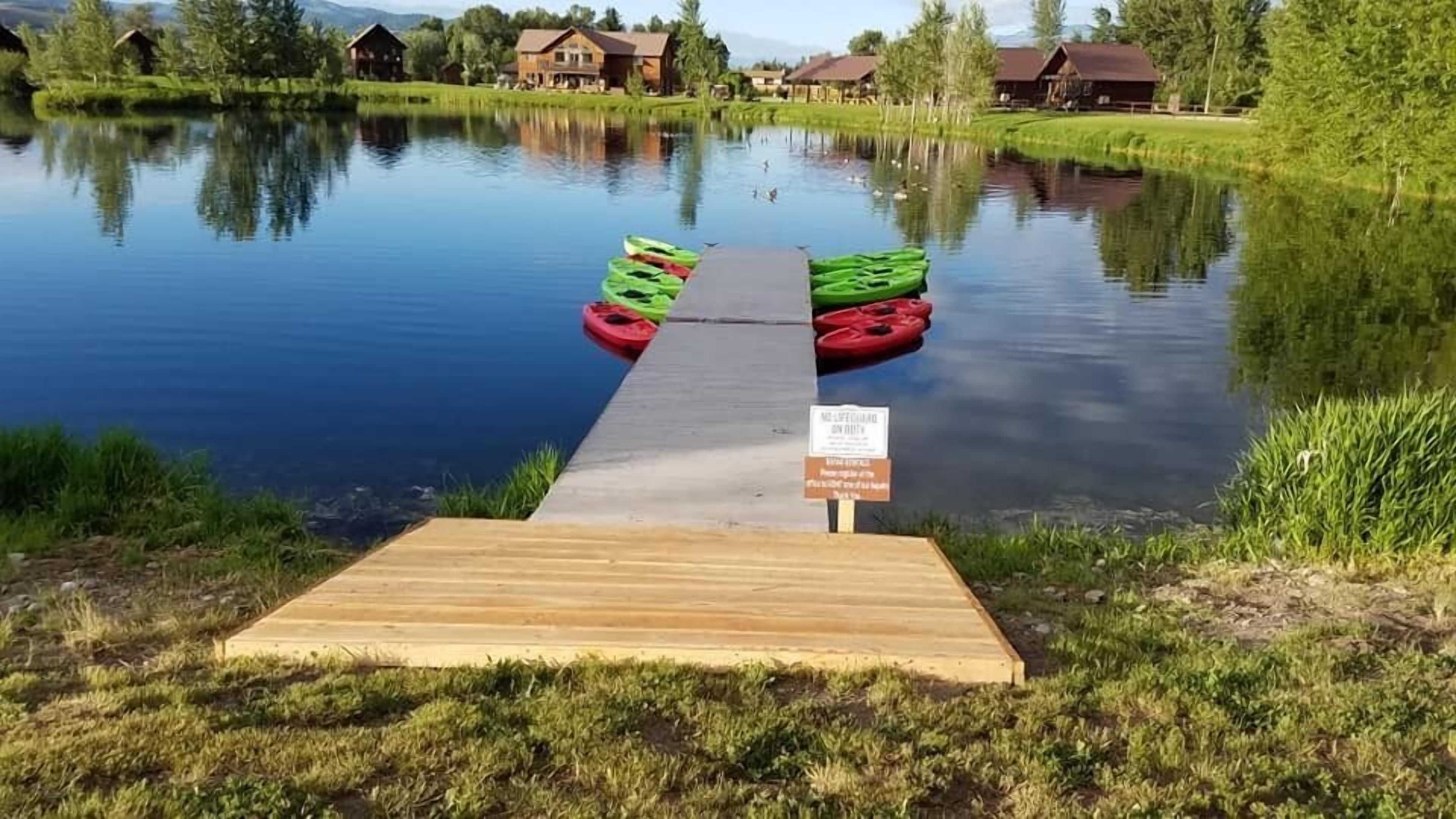 A wooden dock leading into a calm lake with kayaks and paddleboards on the water.