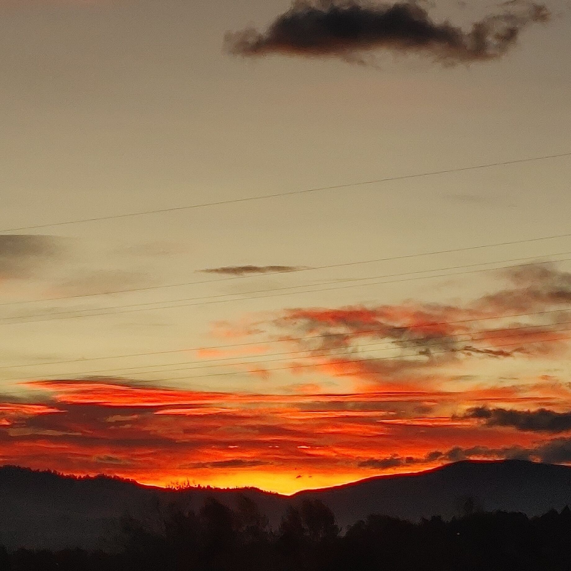 Un atardecer sobre un paisaje montañoso, con líneas eléctricas en primer plano.