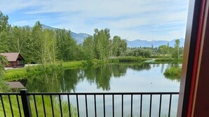 A wooden deck with a metal railing overlooking a calm lake, surrounded by greenery and mountains in the distance. - SkyWater Cabins (Hamilton)