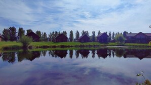 A serene lakeside view with wooden cabins and a large house reflecting on the water. - SkyWater Cabins (Hamilton)