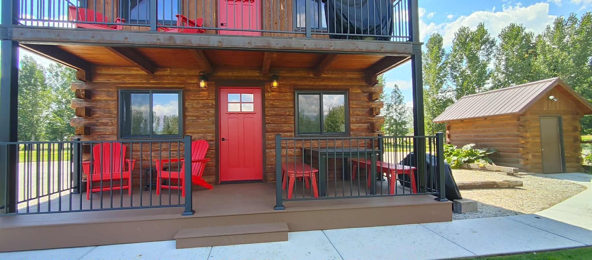 Una cabaña de troncos con balcón, sillas rojas y una pequeña mesa exterior.