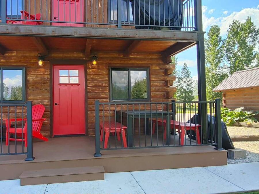 Una cabaña de troncos con balcón, sillas rojas y una pequeña mesa exterior.