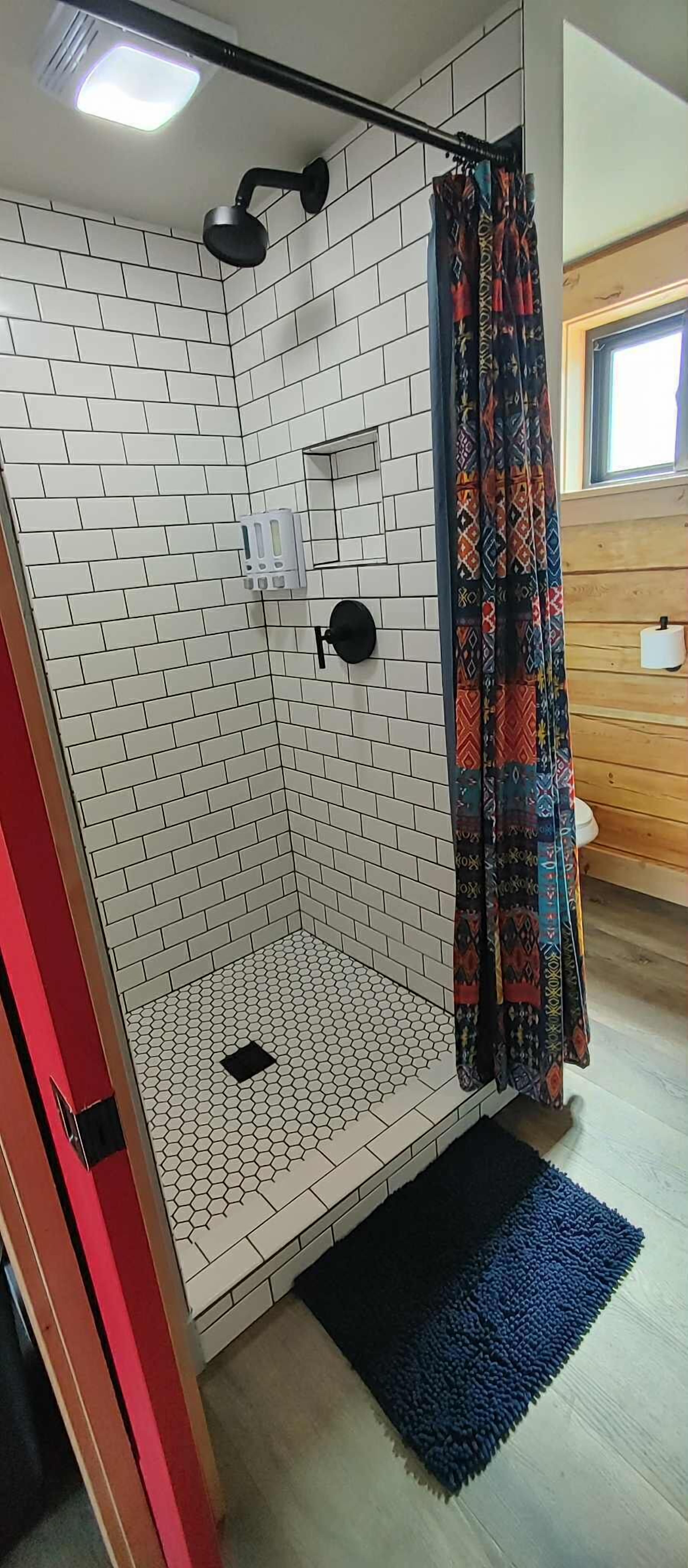 A shower area with white patterned tiles, a black showerhead, and a colorful curtain.