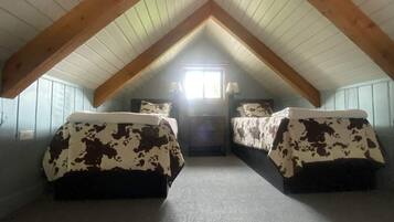 Ein kleines Schlafzimmer im Dachgeschoss mit zwei Betten, einem Fenster und einer Holzzahl.