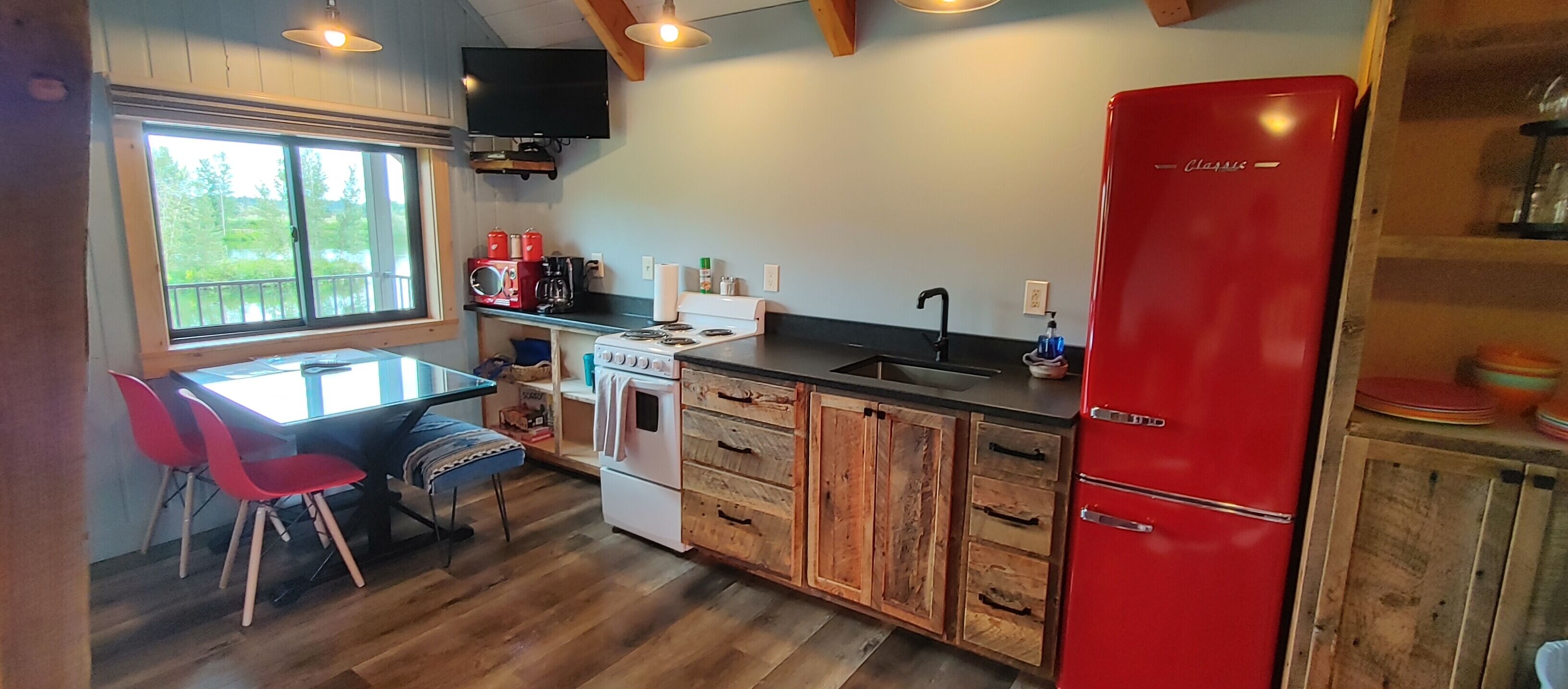 A kitchen with a red refrigerator, wooden cabinets, a white stove, and a dining area with red chairs.