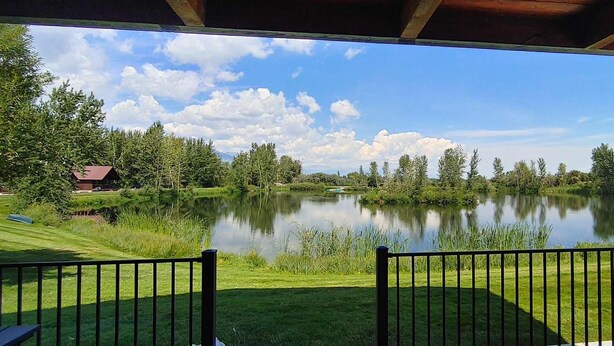 A view from a covered porch overlooking a calm lake with a grassy area and trees in the background. - SkyWater Cabins (Hamilton)