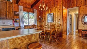 A wooden cabin interior with a dining area, kitchen, and a large window.