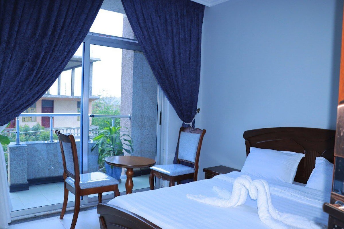 A hotel room with a bed, a chair, a small table, and a view of the outside balcony.