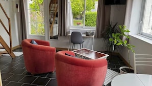 Une pièce chaleureuse avec deux fauteuils rouges, une petite table et un téléviseur fixé au mur.