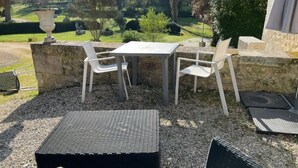 Une terrasse extérieure avec une table et des chaises, entourée d’un jardin agrémenté d’un mur en pierre et de verdure.