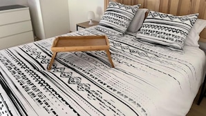 Un lit avec une couvre-lit à motifs, deux oreillers, un plateau en bois et une table de chevet avec une lampe.