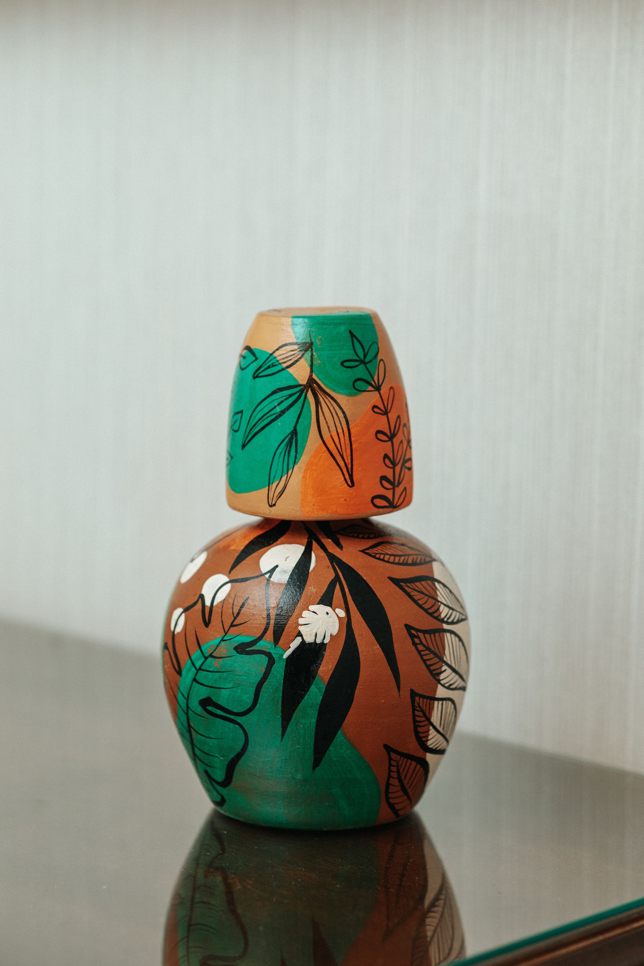 A small, intricately painted ceramic object with a geometric pattern, placed on a reflective surface.