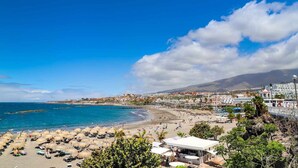 A coastal town with a beach, thatched umbrellas, and a mix of residential and commercial buildings.
