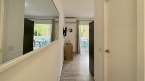 A narrow hallway with a wooden floor, leading to a dining area with blue chairs and a table.