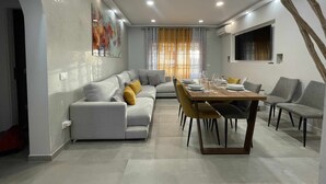 Un espace de salle à manger moderne, avec une longue table dressée pour six personnes, entourée de canapés et de fauteuils gris.