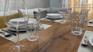 Une table à manger dressée avec de la vaisselle en verre transparent, des assiettes et des couverts, avec une table en bois et un canapé en arrière-plan.