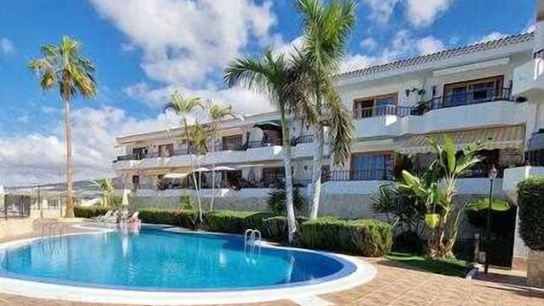 Un hôtel doté d’une piscine, de palmiers et surplombant un ciel bleu azur.