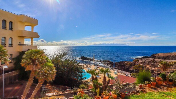 Une vue sur la côte, avec une piscine, des palmiers et un bâtiment doté de balcons donnant sur la mer.