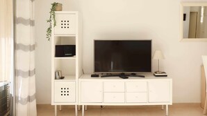 Un salon moderne avec un téléviseur à écran plat posé sur un meuble blanc, une petite plante et une lampe.