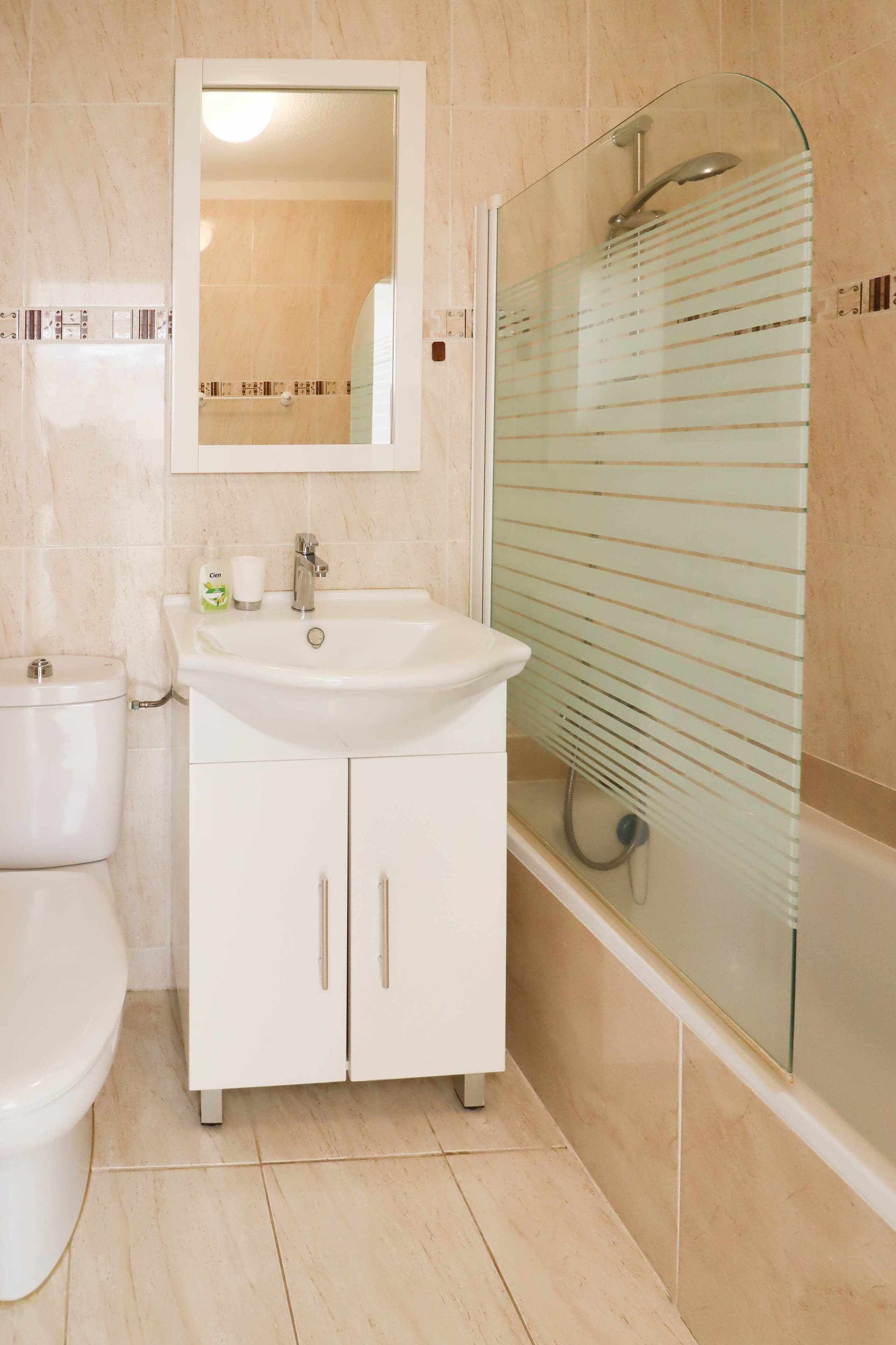 Une salle de bain avec un lavabo blanc, un miroir au-dessus, des toilettes et une douche en verre.