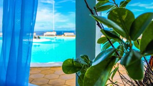 Une vue sur une piscine, aperçue à travers une fenêtre ornée de rideaux bleus, le tout entouré de verdure.