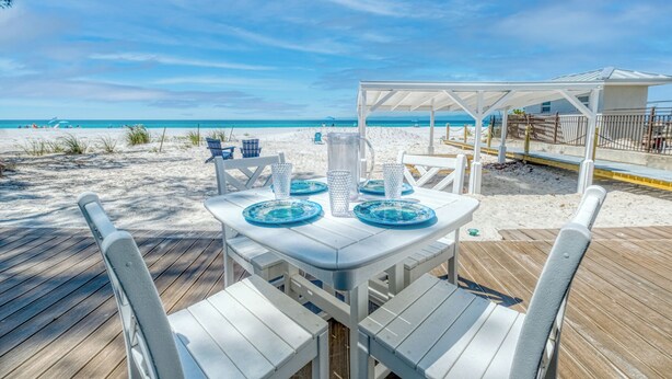 A beachside dining area with a white table and chairs, a covered seating area, and a view of the ocean.