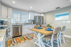 Une cuisine moderne avec des meubles blancs, des appareils en acier inoxydable, une table à manger en bois et un tapis coloré.
