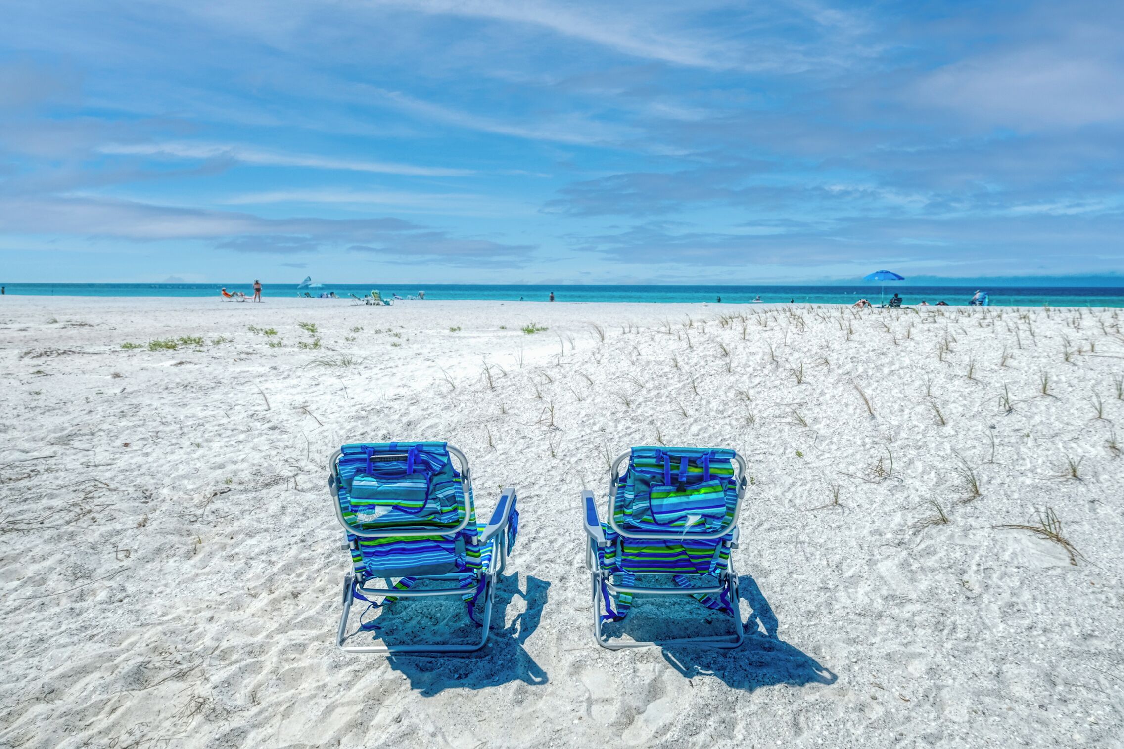 Deux chaises de plage sur une plage de sable, sous un ciel dégagé.