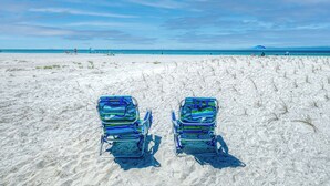 Two beach chairs on a sandy beach with a clear sky.