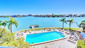 A pool area with lounge chairs and a view of the water. - Waterfront Views~ Heated Pool~ Walk to Beach~ Palms of Treasure Island 210 (Treasure Island)