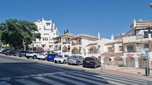 Vista de una calle con autos estacionados, un paso de peatones y edificios con balcones y carteles de un supermercado.