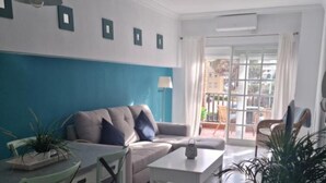 Una sala de estar moderna con sofá, mesa de centro y sillas. Se ve un ventanal con cortinas, y a través de la ventana se divisa un balcón.