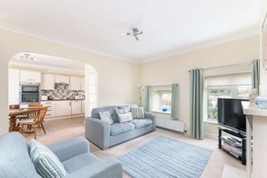 A living room with a sofa, a TV, and a dining area with a table and chairs. - Between Coast & Moors • Pickering 2BR • Sleeps 4 (Pickering)
