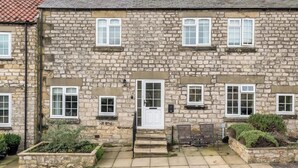 A stone building with a white door and windows, a small porch, and a garden area. - Between Coast & Moors • Pickering 2BR • Sleeps 4 (Pickering)