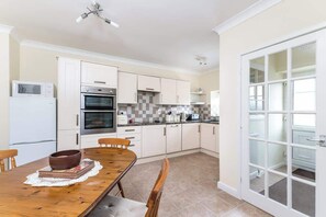 A kitchen with white cabinets, a dining table with chairs, a microwave, an oven, and a large window. - Between Coast & Moors • Pickering 2BR • Sleeps 4 (Pickering)