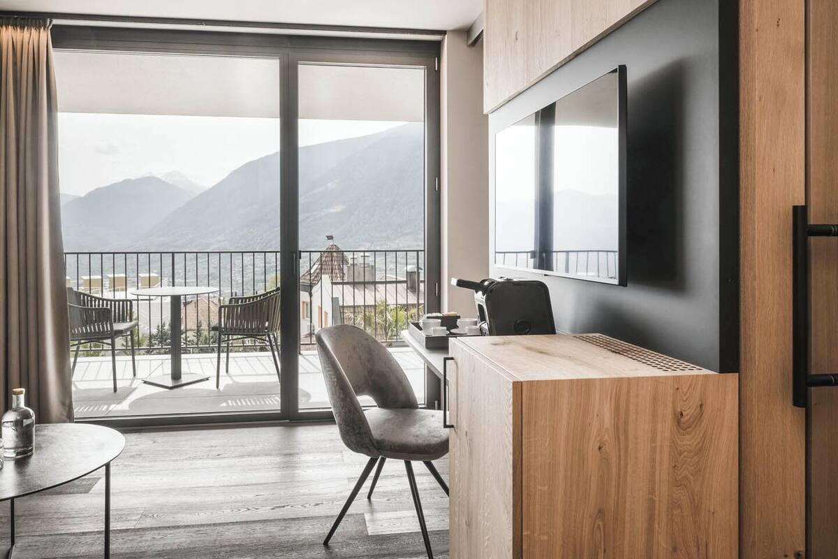 A hotel room with a balcony, a desk, a chair, a bed, and a TV.