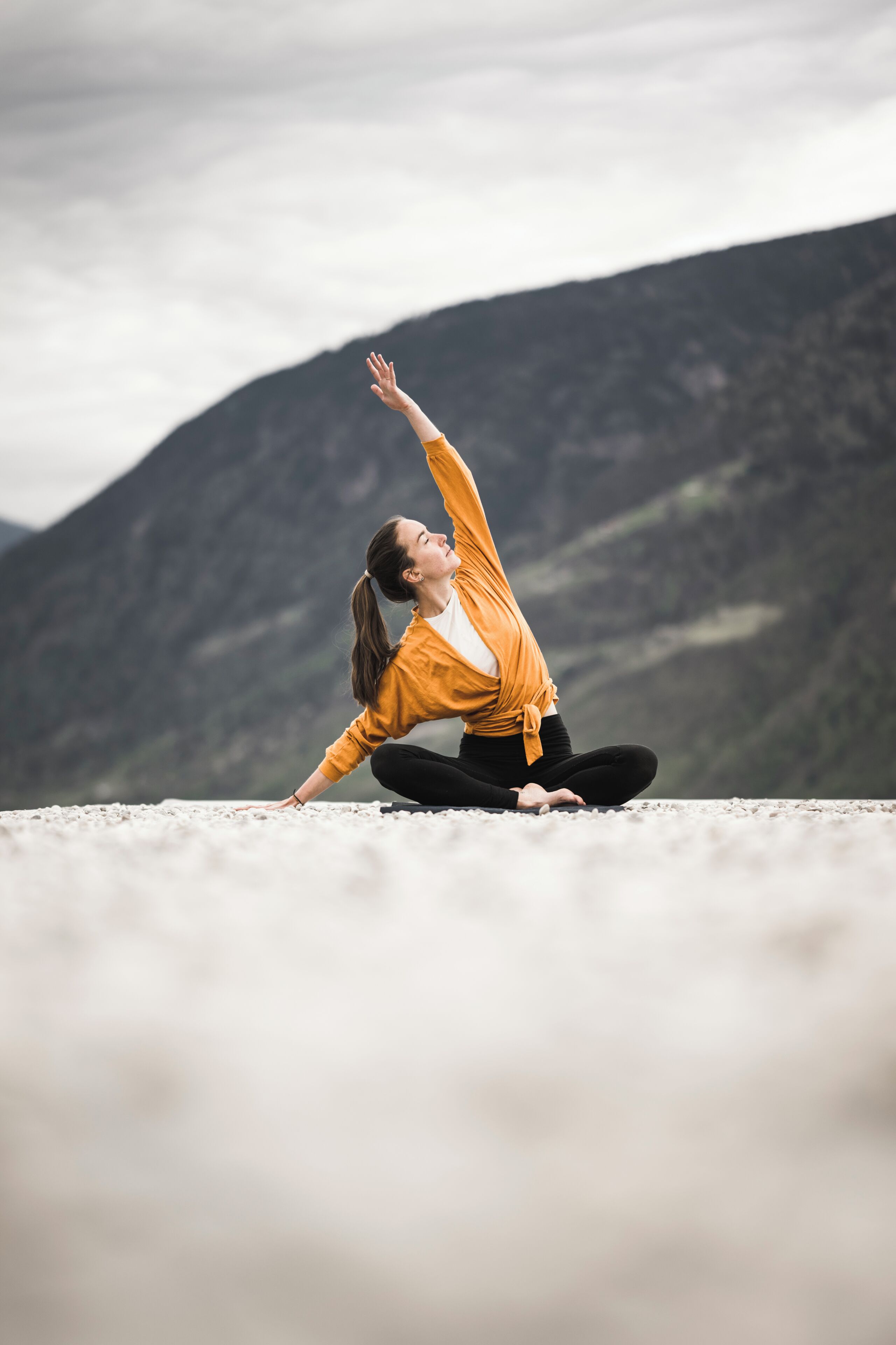 A person in a yoga pose on a beach with mountains in the background.