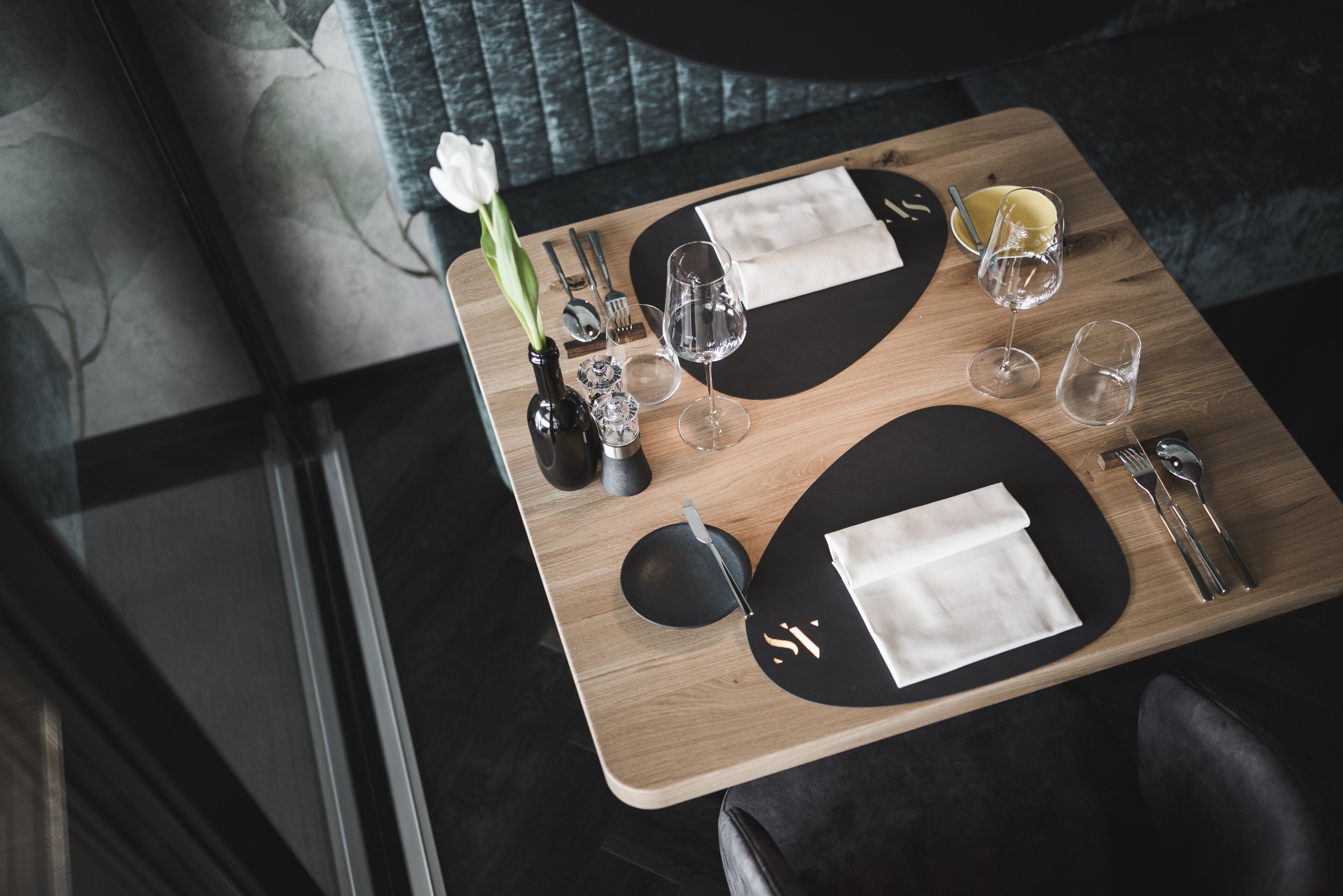 A dining table set with a vase of white flowers, wine glasses, and cutlery.