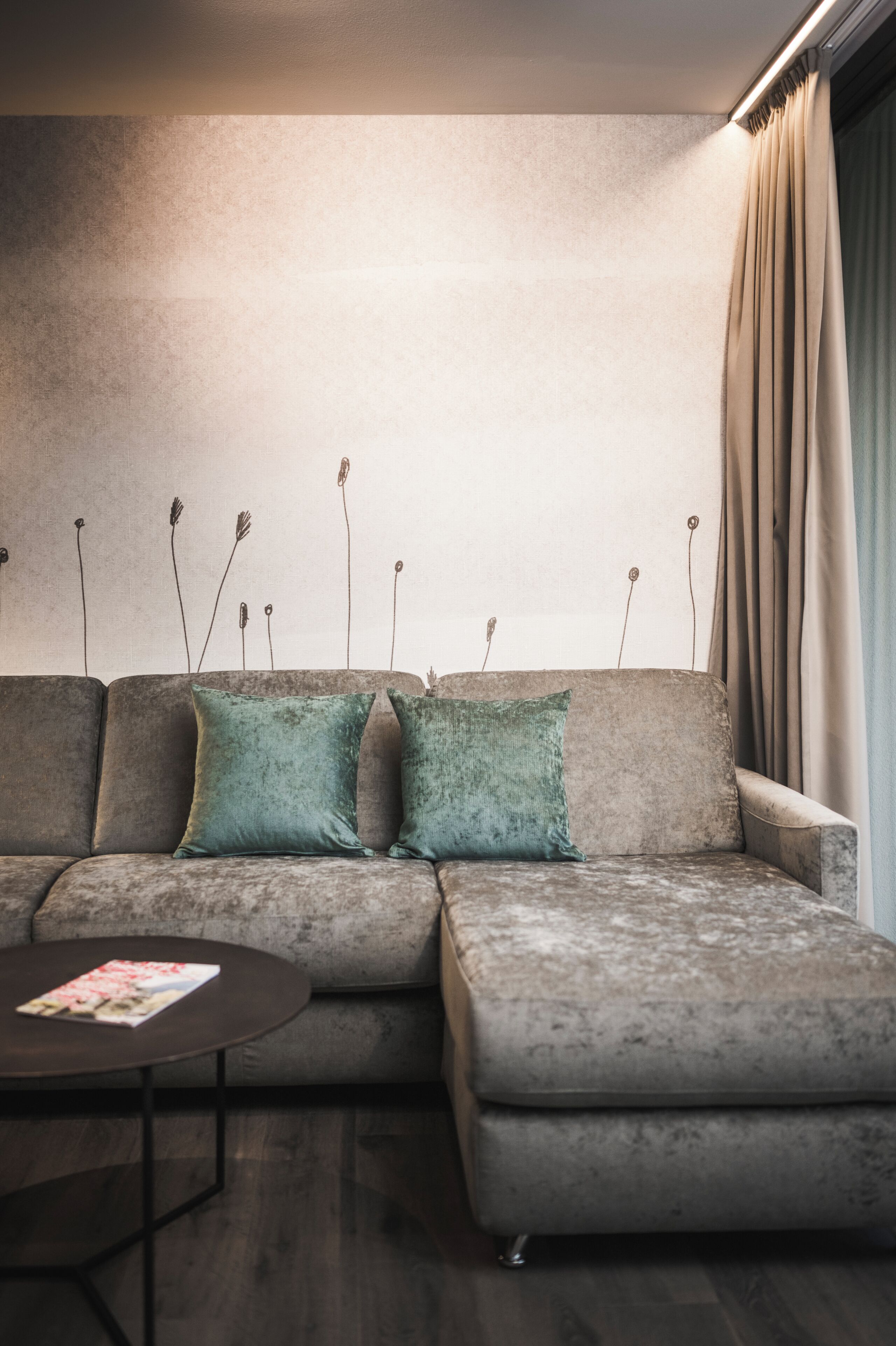 A modern living room with a sectional sofa, two green cushions, a small round coffee table, and a wall with a textured pattern.