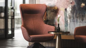 Un interior moderno con un sillón tapizado rojo, una pequeña mesa redonda con un florero y un cuadro abstracto grande en la pared.
