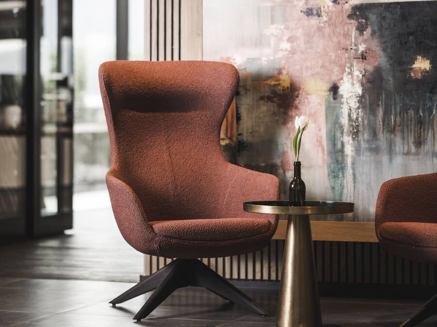 Un interior moderno con un sillón tapizado rojo, una pequeña mesa redonda con un florero y un cuadro abstracto grande en la pared.