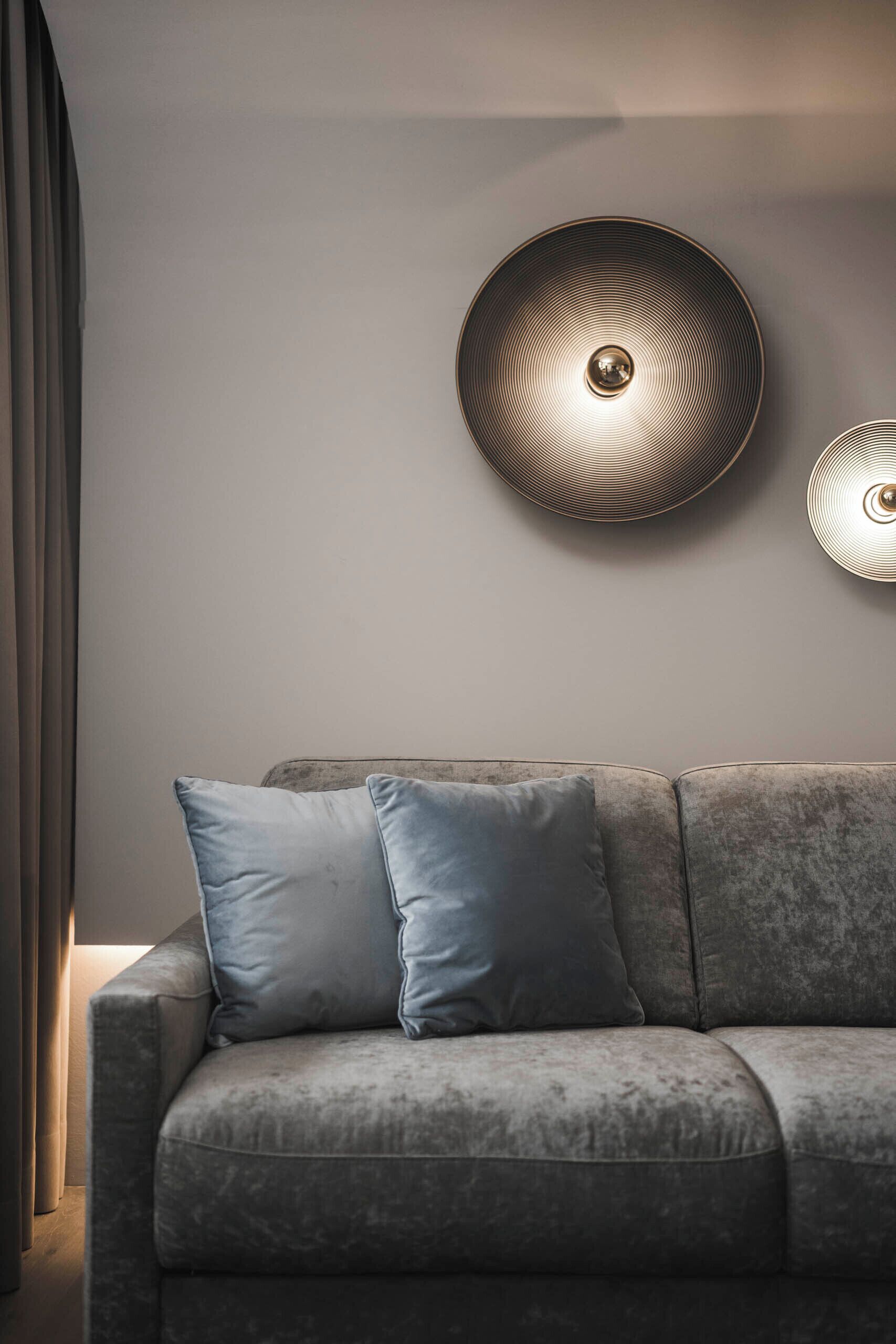Una sala de estar moderna con un sofá gris, dos cojines y dos lámparas fijadas a la pared.