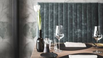 Une table à manger avec un set de table noir, une serviette blanche, deux verres à vin, une bouteille et un vase contenant des fleurs blanches.