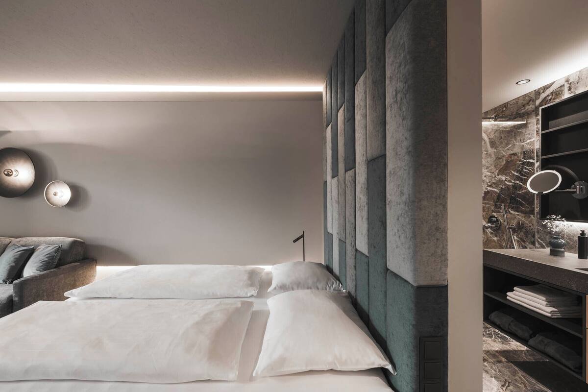 A modern bedroom with a large bed, a sofa, and a vanity with a mirror.