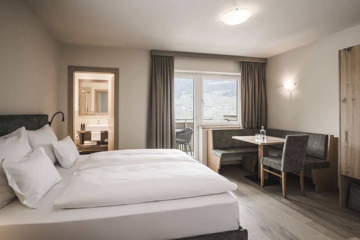 A hotel room with a bed, a desk, a chair, a window with curtains, and a view of the outdoors.