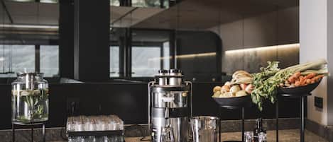 A modern kitchen with a coffee machine, a water dispenser, and fresh vegetables on the counter.