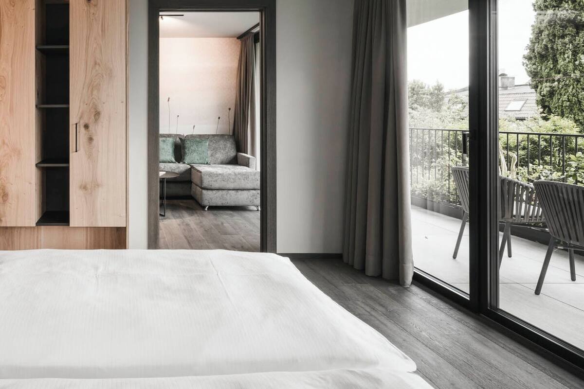 A modern bedroom with a large bed, wooden wardrobe, and a balcony with outdoor seating.